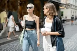Δύο γυναίκες απολαμβάνουν καφέ και συζήτηση σε καλοκαιρινή βόλτα στο κέντρο της πόλης, συμβολίζοντας την ελευθερία από το άγχος υγείας μέσω κοινωνικών δραστηριοτήτων και χαλάρωσης μετά από ομοιοπαθητική θεραπεαί στην Αθήνα