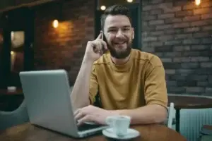 Χαμογελαστός άνδρας εργάζεται παραγωγικά σε laptop με καφέ χωρίς ημικρανία ή πονοκέφαλο χάρη στην ομοιοπαθητική θεραπεί στην Αθήνα