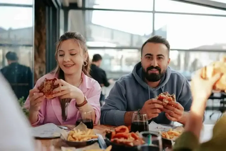 Alt Text: Ζευγάρι απολαμβάνει burger και τηγανητά σε εστιατόριο χωρίς φόβο για καούρα ή παλινδρόμηση χάρη στην ομοιοπαθητική θεραπεία για γαστροοισοφαγική παλινδρόμηση στην Αθήνα