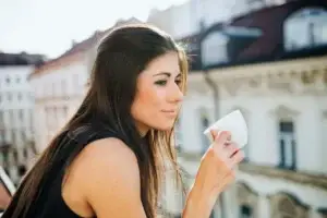 Γυναίκα 30 ετών πίνει καφέ σε μπαλκόνι αναπνέει ελεύθερα μετά από ομοιοπαθητική θεραπεία χρόνιας ιγμορίτιδας στην Αθήνα.