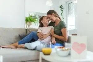 Μητέρα και κόρη χαμογελαστές στον καναπέ - Βελτίωση ποιότητας ζωής στην ελκώδη κολίτιδα με ομοιοπαθητική