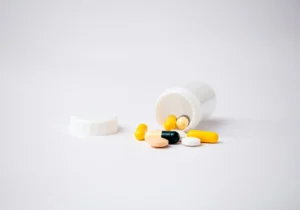 Ανοιχτό δοχείο με κάψουλες αντιβίωσης και χάπια σε λευκό φόντο, συμβολίζοντας τη φαρμακευτική αγωγή.