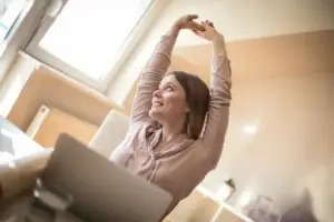 Γυναίκα εργαζόμενη στο γραφείο κάνει διατάσεις χεριών νιώθοντας ανακούφιση από το Σύνδρομο Γραφείου και τους μυϊκούς πόνους